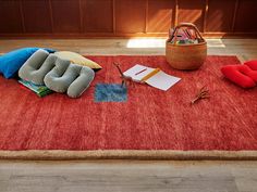 a red area rug with pillows, books and other items laying on top of it