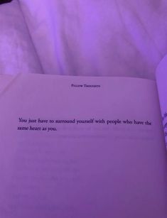 an open book sitting on top of a bed next to a purple light and pillows