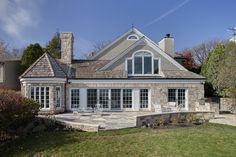 a large house with a stone patio and white chairs in the front yard, on a sunny day