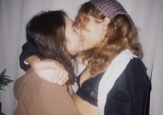 two women are kissing each other in front of a white curtain and a potted plant