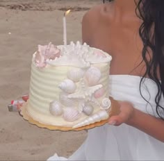 a woman holding a cake with seashells on it and a candle in the middle