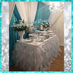 the table is set up for an event with blue and white drapes, chandelier, and vases filled with flowers