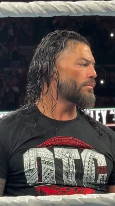 a man with long hair wearing a black shirt and standing in the middle of a wrestling ring