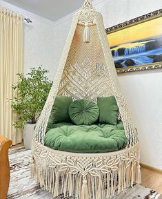 a white hanging chair with green cushions and tassels on the bottom, next to a potted plant