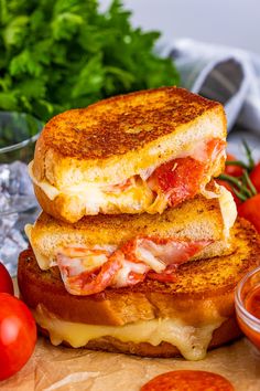 two grilled cheese sandwiches stacked on top of each other next to tomatoes and ketchup