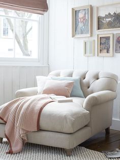 a living room with white walls and pictures hanging on the wall, a chair in front of a window