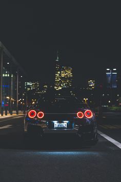 the back end of a black sports car in front of a city skyline at night