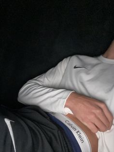 a man laying on top of a black couch wearing a white shirt and blue pants