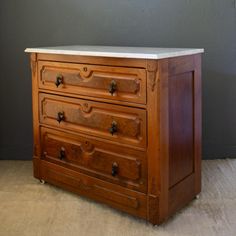 an old wooden chest of drawers with marble top on carpeted floor next to gray wall