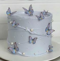 there is a white cake with blue butterflies on the top and pearls on the bottom