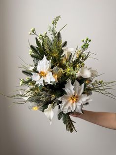 a bouquet of flowers being held by someone's hand in front of a white wall