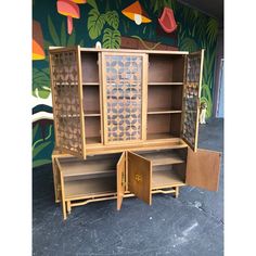 a wooden cabinet with glass doors and drawers in front of a colorful wallpapered background