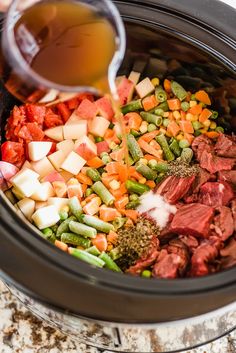 someone pouring sauce into a slow cooker filled with meat, vegetables and seasonings