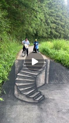 two people riding bikes down a road with a spiral staircase on the side and trees in the background