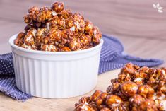 a white bowl filled with caramel popcorn on top of a wooden table next to a blue towel