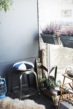 an outdoor balcony with plants and stools on the floor, next to a window