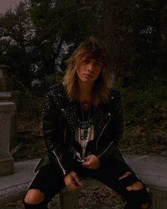 a man with long hair and piercings sitting on a bench in front of a cemetery