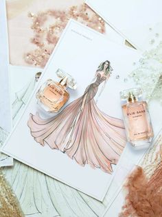 two bottles of perfume sitting on top of a table next to an envelope with a drawing of a woman in a dress