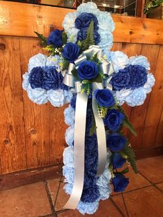 a cross decorated with blue flowers and white ribbon hanging from the side of a wooden wall