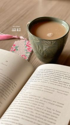 an open book sitting on top of a wooden table next to a cup of coffee