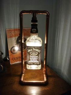 a bottle of alcohol sitting on top of a wooden table next to a book and lamp