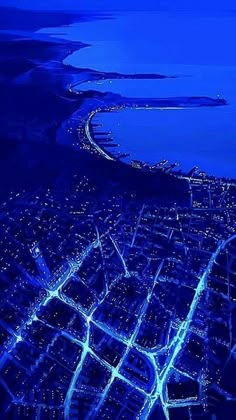 an aerial view of a city at night with lights on the streets and water in the background