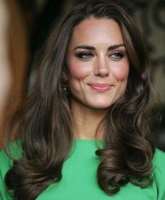 a woman with long brown hair wearing a green dress and smiling at someone in the background