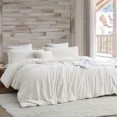 a white bed sitting in a bedroom next to a wooden headboard with windows on each side