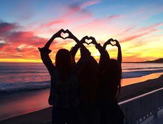 two girls making heart shapes with their hands on the beach at sunset or sunrise time