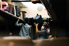 two people are working on an object in a room full of other people and one person is holding it up