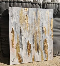 a painting with gold paint on it sitting next to a gray couch and pillows in the background