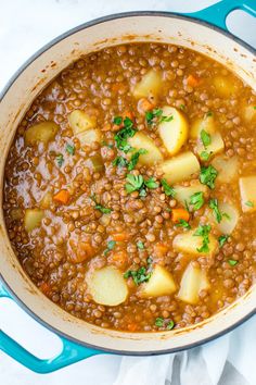 a pot filled with lentils and potatoes on top of a white cloth next to a blue spoon