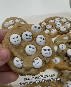 a person holding up a cookie with white chocolate chip eyes and faces on it in front of other cookies