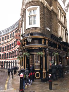 people are standing on the sidewalk in front of an old fashioned building that has been converted into a restaurant