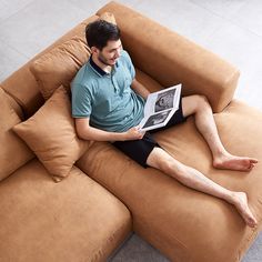 a man sitting on top of a brown couch holding a magazine in his hand and looking at it