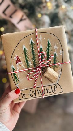 someone holding up a wrapped present in front of a christmas tree