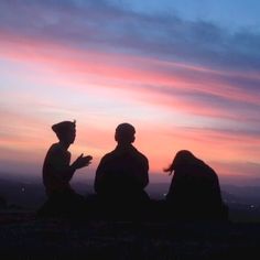 two people sitting on the ground in front of a sky with pink and blue clouds