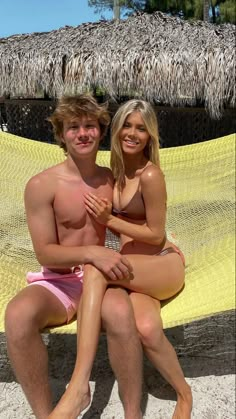 a man and woman sitting on a hammock at the beach, posing for a photo