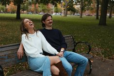 a man and woman sitting on a park bench laughing at each other's side