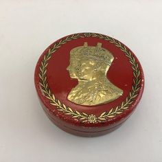 a small red box with a gold crown on the lid and a wreath around it