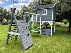 a wooden swing set with a slide and climbing frame in the grass next to trees