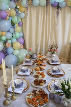 a table set up for a tea party with desserts and balloons in the background