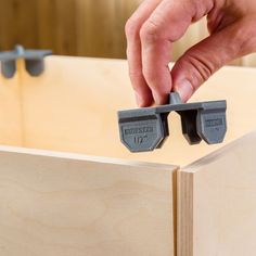 a person holding two pieces of wood in front of a wooden box with screws on it