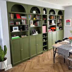 a dining room with green bookcases and wooden floors