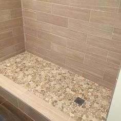 a tiled shower stall with brown and tan tile on the floor, along with a gray rug