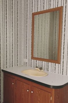 a bathroom vanity with a mirror and sink in front of striped wall papered walls