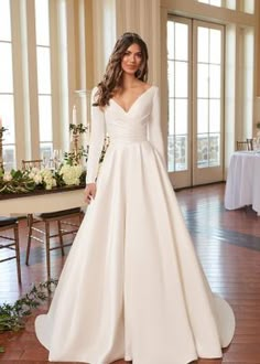 a woman standing in front of a table wearing a wedding dress with long sleeves and pockets