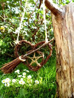 a heart shaped wicker hanging from a tree in the grass next to some flowers