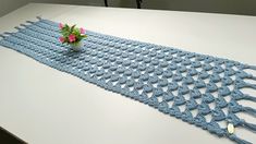 a blue crocheted table runner with flowers in a vase on it, sitting on a white surface