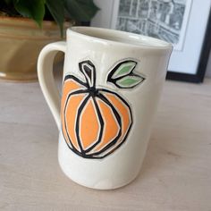 a white coffee cup with an orange painted on it